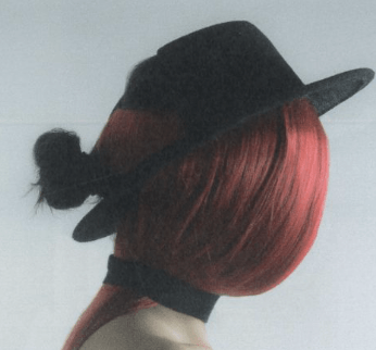 Person with long, straight red hair wearing a black hat and black choker, facing sideways with hair covering their face.